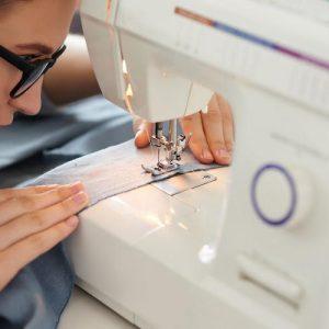 Young woman closely looking how sewing machine works